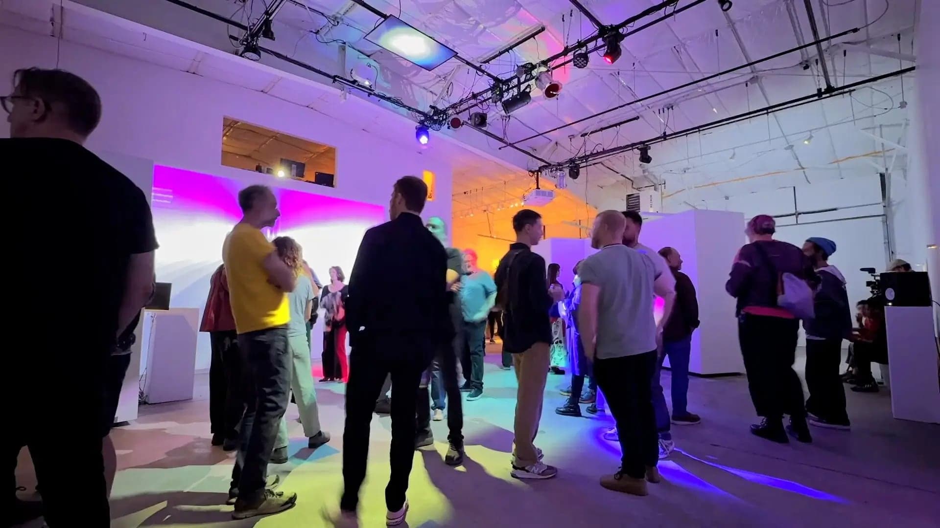 A fan of pale blue projected light unfolding across a gallery wall beside speakers and a sensor pedestal